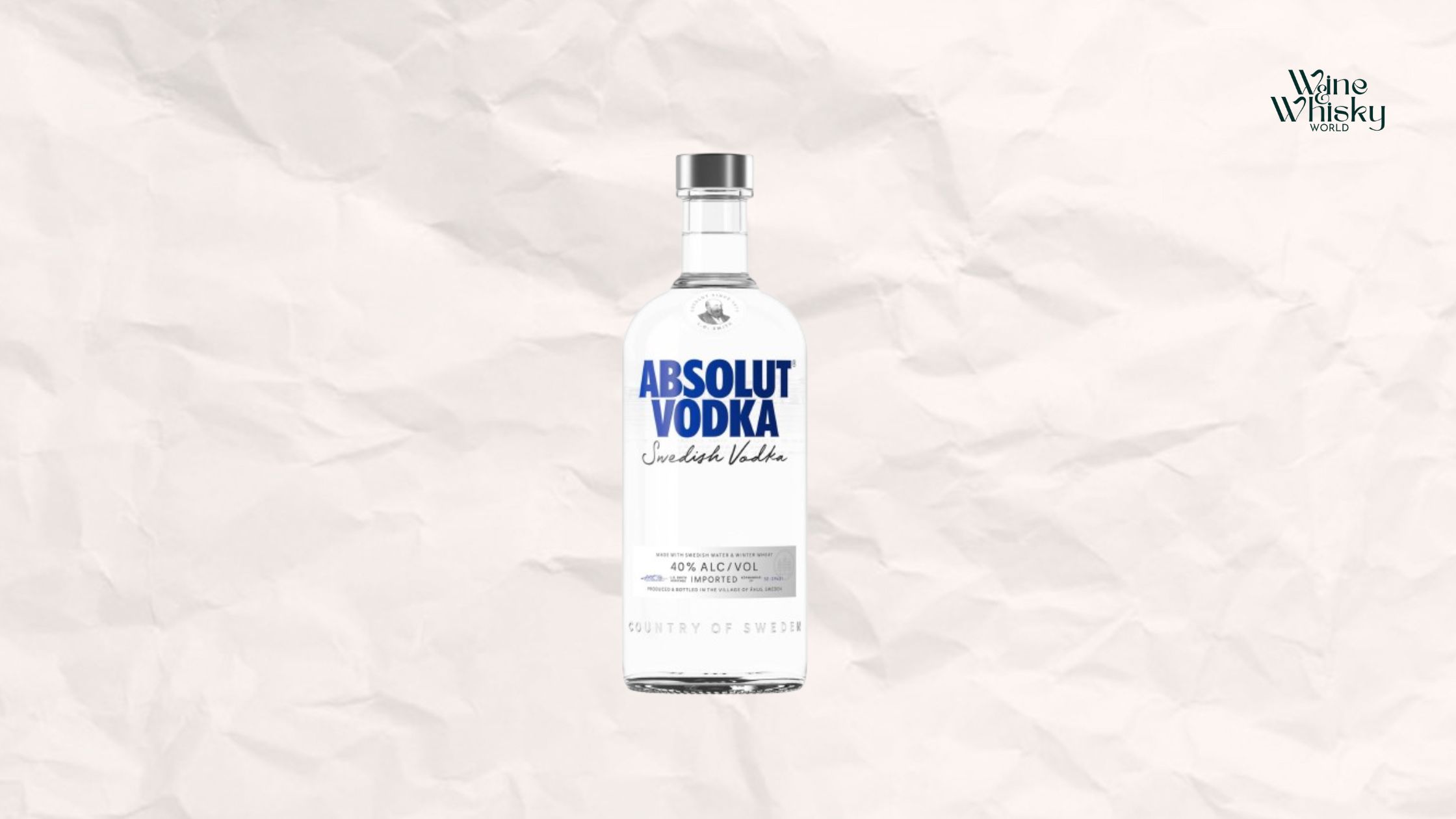Clear glass bottle of Absolut Vodka with blue and black text on the label, reading 'Absolut Vodka Swedish Vodka', displayed against a crumpled white paper background with the Wine Whisky World logo in the top right corner.